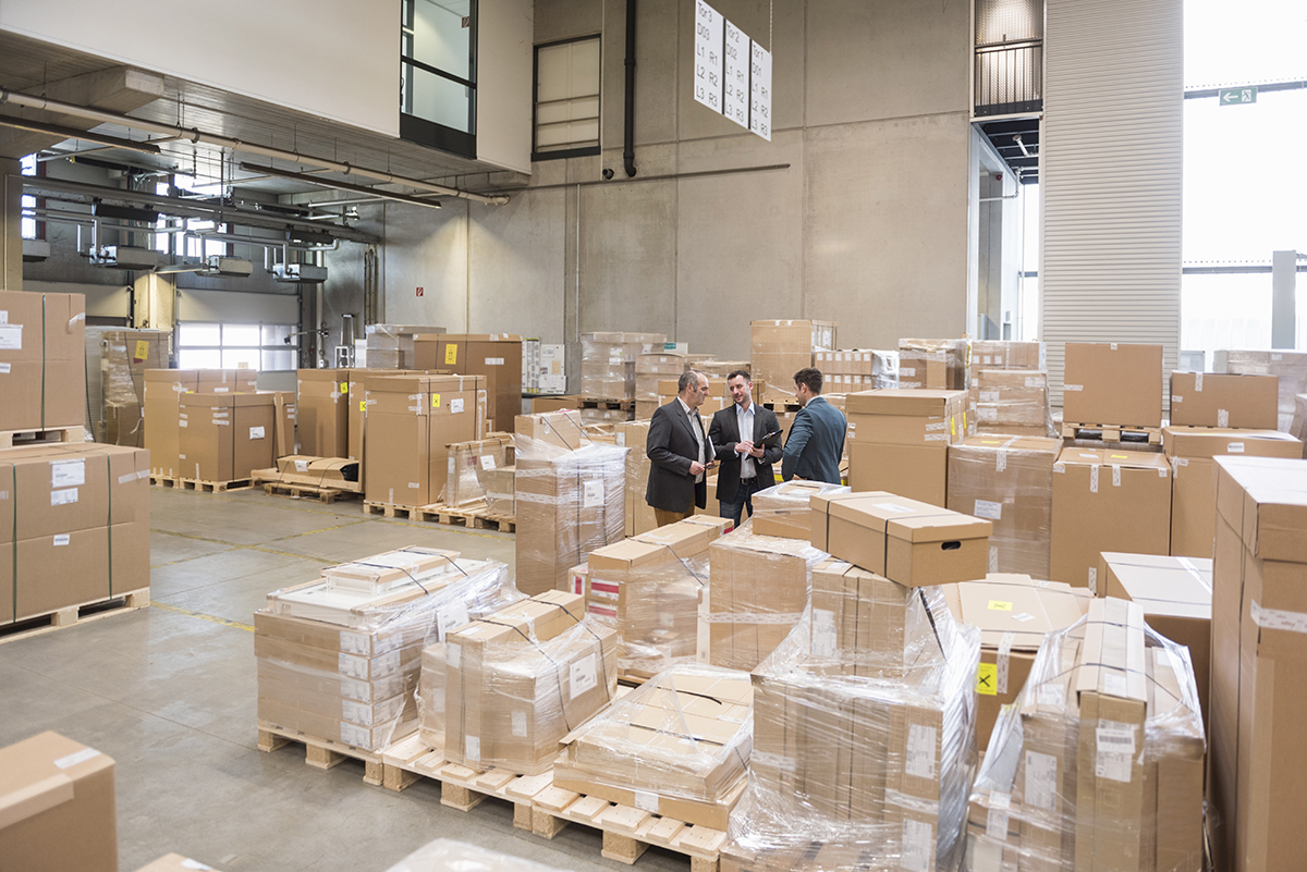 Three men in factory warehouse surrounded by cardboard boxes Three men in factory warehouse surrounded by cardboard boxes