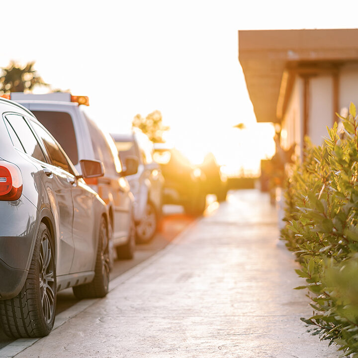 Row of cars parked near the sunny sidewalk in front of the house parking lot security